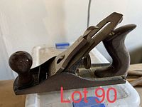 Metal hand plane with wooden handles, dark patina, resting on a surface
