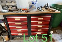 Full front view of work bench with two columns of red drawers with labels, some tools on top and plastic container.