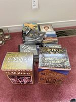 Full lot photo showing stacked CDs and two boxed DVD series sets on carpet.