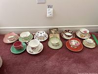 Full view of all ten cups and saucers lined up on floor showing variety in design and condition.