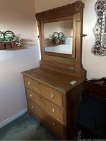 Full view of antique wooden dresser with three drawers, porcelain knobs, and attached swinging mirror with decorative details.