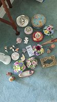 Top view of assortment of figurines and trinket boxes on blue carpet showing various floral and animal figures and small decorative boxes.