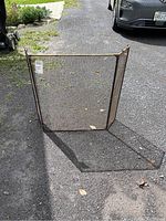 Front view of the three panel brass-look fireplace screen showing mesh and rust spots.