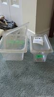 Two clear plastic food service containers of different sizes with lids, one container lid has a label sticker attached.