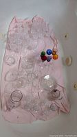Wide view of the glass and crystal stemmed glasses, colored glass pieces, and clear glass plates laid on pink cloth.
