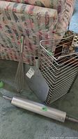 Photo showing the kitchen items including metal rolling pin, whisk, pizza paddle, and metal pan rack placed on carpet near a couch.