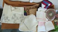 Overview of a variety of folded linens on a wooden surface, showing different tablecloths, placemats, and hand towels in various shades and patterns.