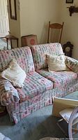 Full front view of the loveseat couch showing multicolor patterned upholstery, two white throw pillows, and skirted base.