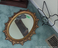 Oval wall mirror with ornate gold-tone frame showing measurement sticker 17x14 inches, placed on carpeted floor.