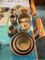 Photo showing the various ceramic serving pieces including the teapot, covered butter dish, cream and sugar set, small pitchers, sauce boat, bean pot, and bowls with Folk Art pattern.