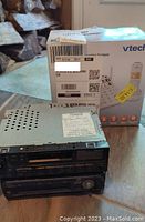Box and VTech cordless phone visible behind two stacked car radios on a wooden surface.