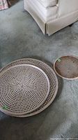Two vented pizza pans on carpet floor near furniture, one large approx. 21", one small approx. 11"