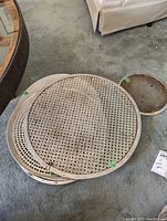 Top view of multiple stacked pizza pans on carpet. Characteristic perforations and mesh patterns visible. Varying sizes from small to large.