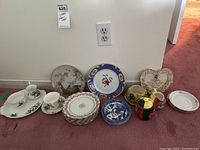 Full assortment of plates, cups, and serving pieces arranged on floor against wall, showing multiple designs and item types.