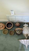 Overview photo showing grouped pottery bowls, jars, and teapot arranged on floor against wall vent.