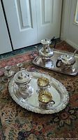 Photo of coffee pot, teapot on tray, covered serving dish, small bowls and large ornate tray on carpet