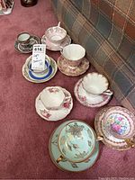 Overview of all 9 teacups and saucers arranged on carpet showing different designs.