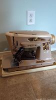 Full side view of vintage Singer sewing machine on beige base with power cord coiled on side.