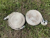 Two large coiled water/fire hoses on grass, showing overall shape and material
