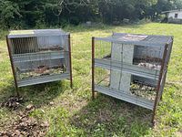 Photo of two multi-level metal cages for small animals in an outdoor grassy area, showing wire mesh bars and galvanized metal panels.