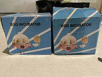 Two blue boxes labeled 'EGG INCUBATOR' showing product branding and graphics featuring eggs and hatching chicks.