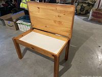 Wooden children’s desk with hinged top open showing white storage compartment inside suitable for materials.