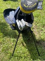 Children's left-handed golf clubs in a blue and yellow golf bag standing on grass, viewed from front with club heads visible.