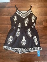 Full view of the black romper laid flat showing front design, straps, floral pattern, and waistband