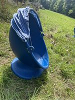 Side view of blue egg chair with fabric canopy hanging and torn, placed on grass