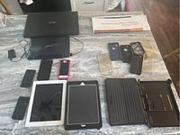 Group of multiple phones, two iPads, cases, and a tablet laid on a table surface