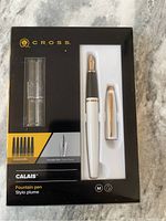 Cross Calais fountain pen set in packaging including pen with black and white body, gold nib and accents, one additional clip, converter, and six black refill cartridges.