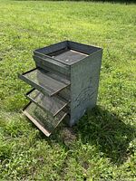 Metal fruit dryer with four pull-out mesh trays outside on grass, showing entire drying rack structure.
