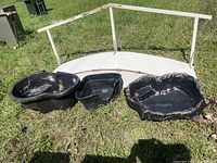 Three black plastic pond liners arranged side by side on grass, shows varying shapes and sizes with some dirt residue.