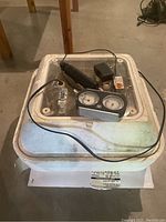 Top view of white foam incubator with clear lid, power cord, thermometer/hygrometer device, and egg candler on top.