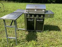 Full view of Kenmore gas BBQ grill with closed stainless steel lid, side table extended, and grass background.