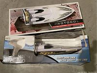 Photo of two Gravity Shore Liner remote control boats, one boxed and one out of box, both showing signs of wear and missing parts.