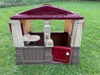 Front view of beige and brown plastic playhouse with a maroon roof, open front door, and interior sink fixture.
