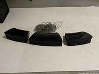 Three black speaker units placed in a row with bundled wires on white surface.