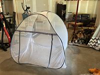 Single small white mesh screen pop-up tent with zippered doorway, set up indoors on a concrete floor.