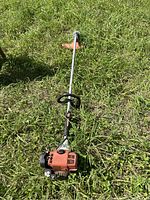 Full length photo of the Stihl weed whacker on the grass showing the entire tool, including engine, shaft, handle, and cutting head with guard.