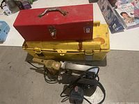 Image showing stacked red metal toolbox on top of large yellow plastic toolbox with two power tools placed in front.