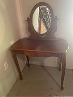 Full view of wooden vanity with oval swivel mirror and curved legs