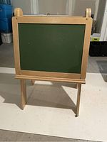 Front side of easel showing the green chalkboard surface and sturdy wooden frame and legs.