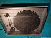 View of the entire turntable inside the transparent dust cover, showing the tonearm, platter mat, and controls beneath the cover.