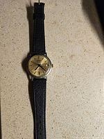 Full watch view with black leather strap and gold-tone face showing general condition and strap details.