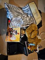 Box containing patterned textile, boxed kitchenware, plush toy dog, and other items.