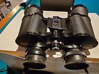 Front view of Bushnell binoculars placed on a white surface showing textured black body and rubber eyecups.