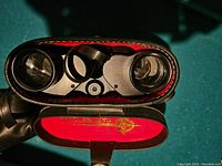Close-up showing the front of the binoculars with lenses and focusing mechanism visible inside the open leather case.