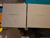 Two grey Liebeskind Berlin branded boxes for belts placed side by side on a surface.