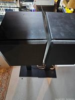 Top view of two black speakers with front fabric covers on black metal stands
